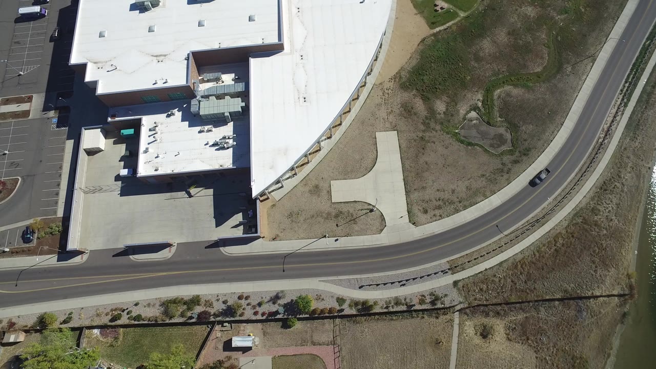 Overhead view of a white-roofed building beside a curved road and water channel.