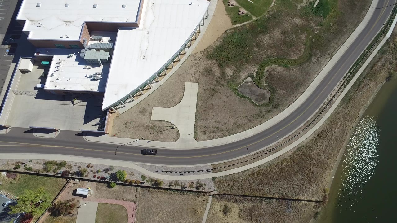 Aerial view of a car on a curved road beside a lake and commercial building.