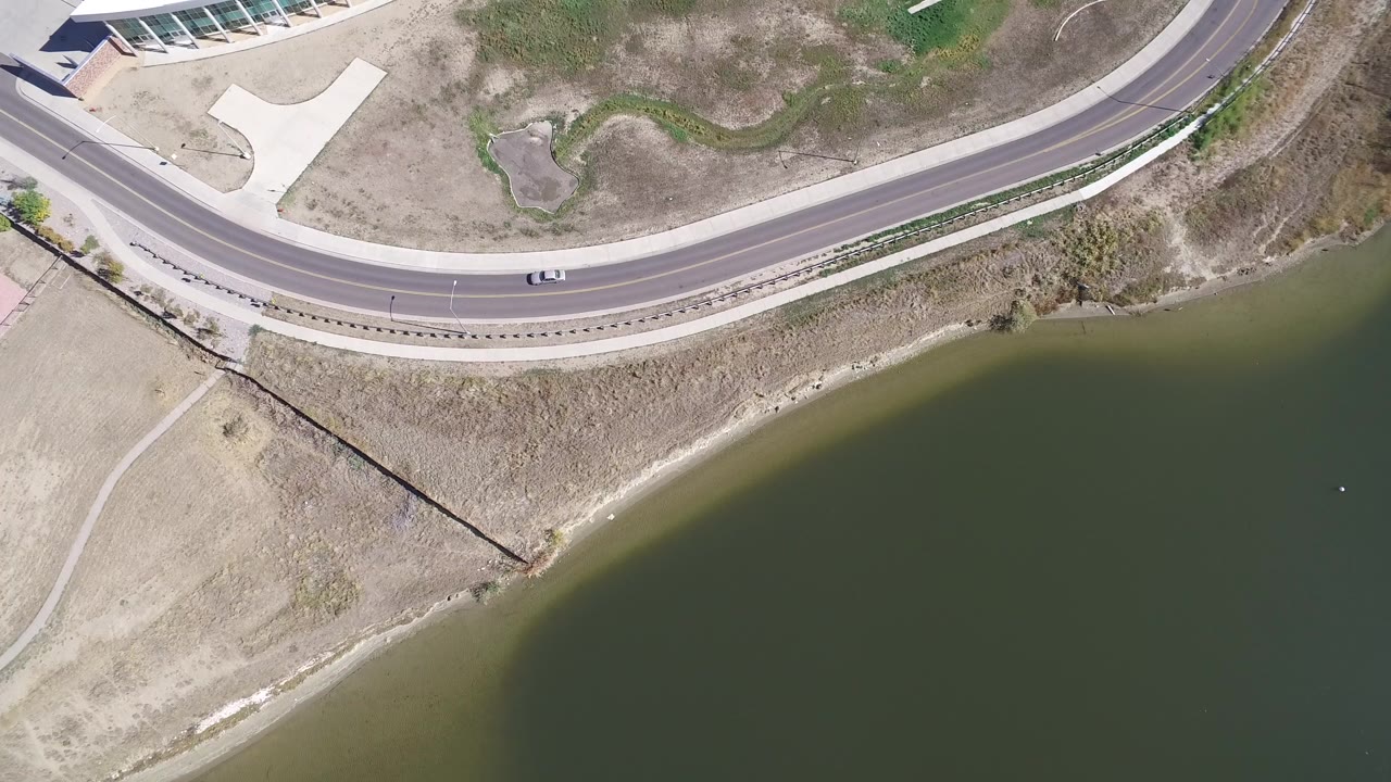 Overhead frame of Hidden Lake, Colorado showing a curved paved road, dry shore, green water, nearby paths, and no visible people.