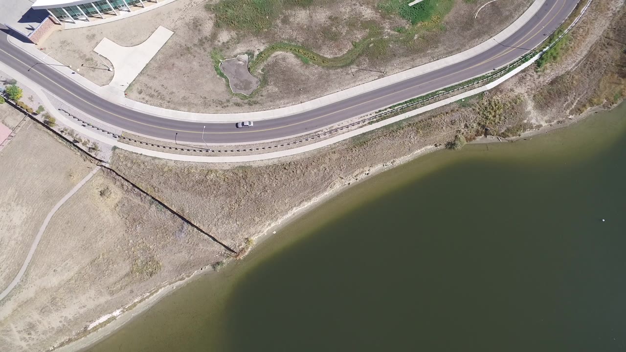 Aerial frame of Hidden Lake, Colorado with a small white car on the curved road above the lake and no visible people.