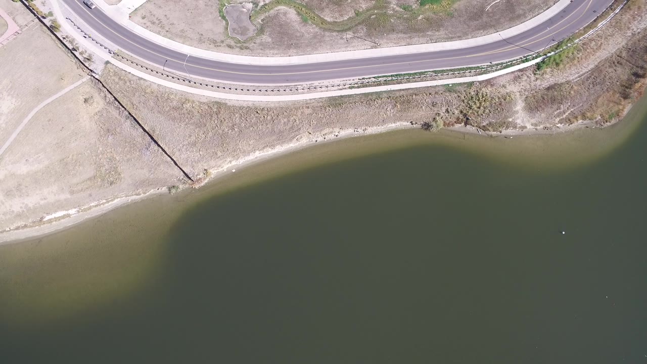 Aerial view of a road bend above an olive-colored lake.