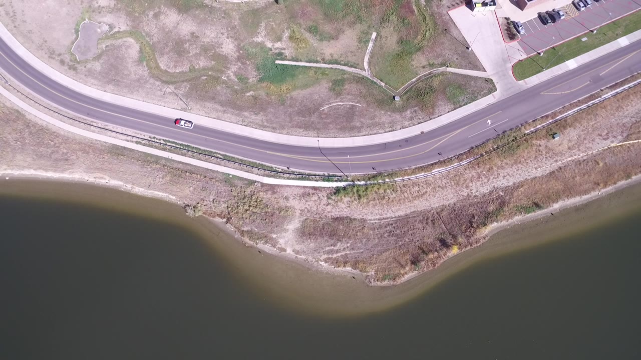 Overhead view of a curved road beside a lake shoreline.