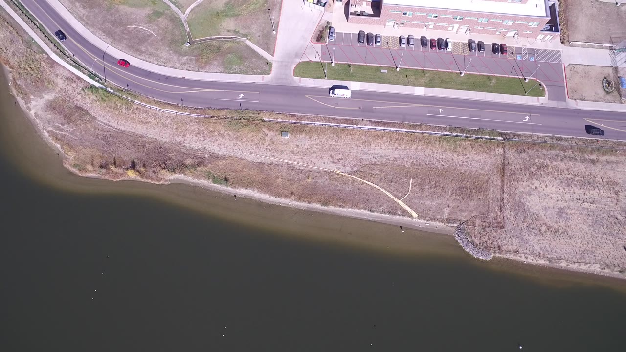 Overhead view of a road beside dark lake water and dry shoreline.