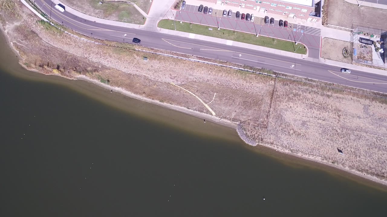 Overhead view of a lake edge, road, and passing cars.