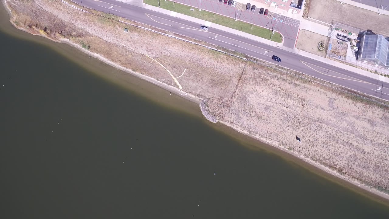Overhead lakeside road beside dark water and pale shoreline.