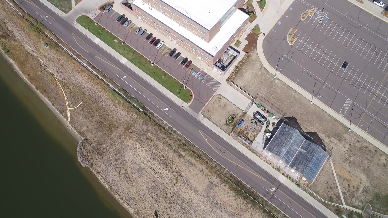 Drone view of road, lake edge, parking lot, and building roofs.