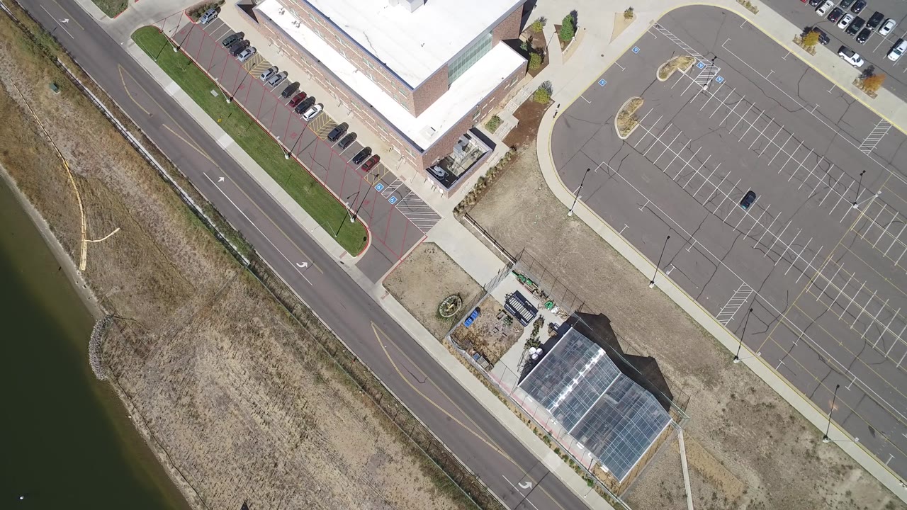Top-down frame of a commercial parking lot, road, building corner, and roadside open land.