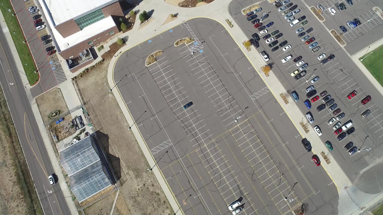 High overhead view of a Hidden Lake, Colorado parking lot with painted stall lines, parked cars along the right side, a road at left, nearby buildings, and no visible people.