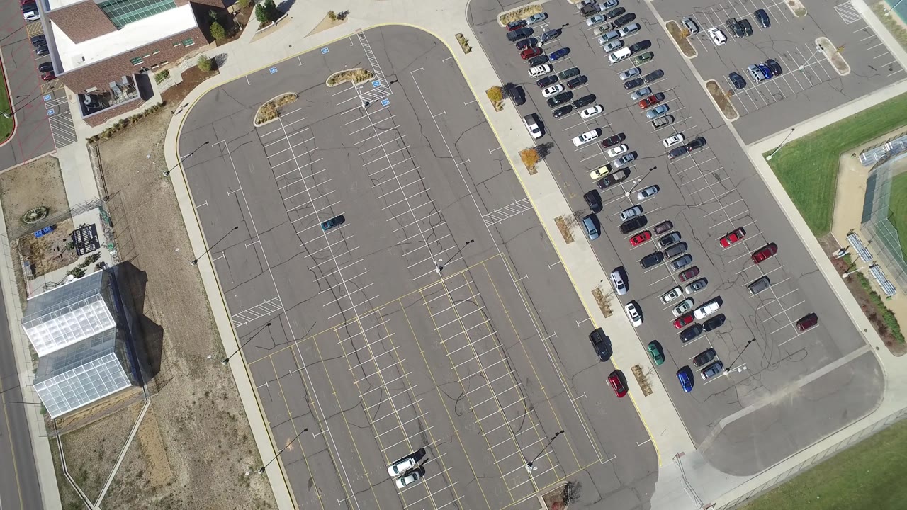 Overhead frame in Hidden Lake, Colorado showing the parking grid centered in view, parked vehicles along the right side, building roofs at the edge, and no visible people.