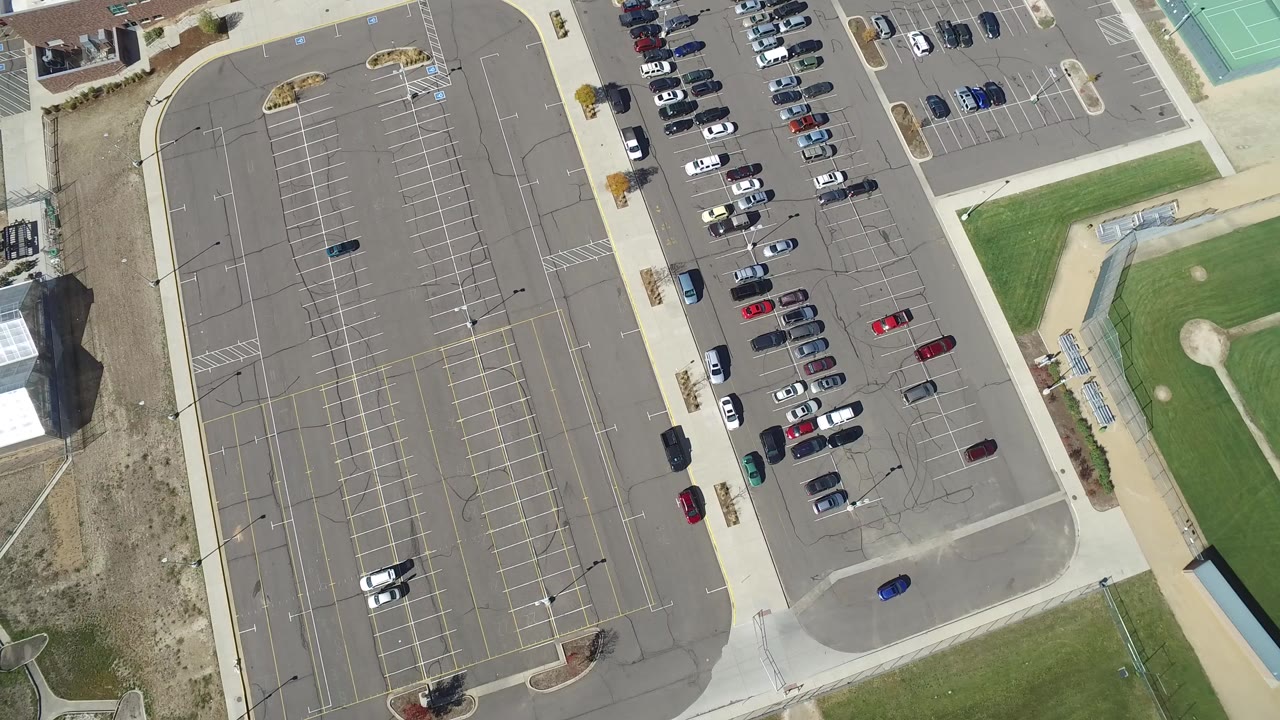 Top-down aerial view of a striped parking lot beside roads and grass fields.