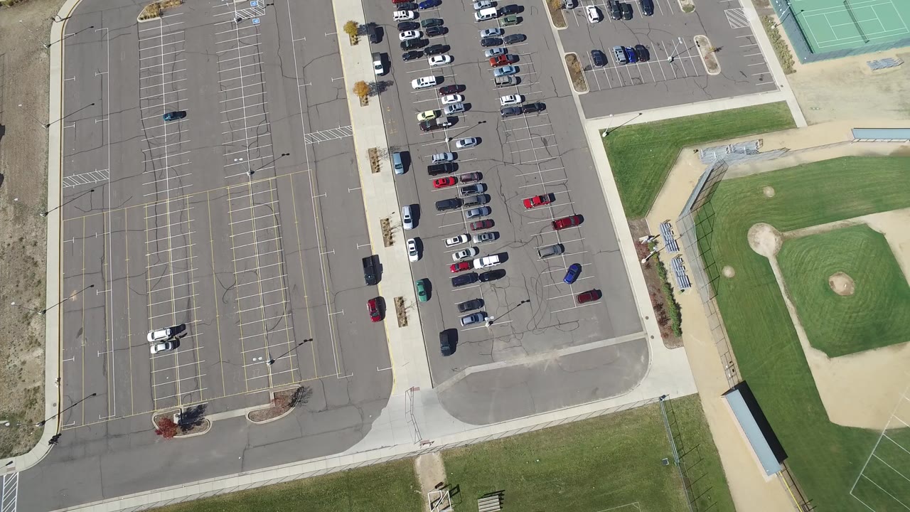 First overhead frame of a Hidden Lake, Colorado sports complex showing marked parking lots, parked cars, baseball diamonds, walkways, tennis courts, and no visible people.
