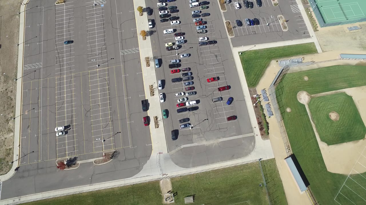 Aerial frame of parking stalls, cars, baseball diamonds, and courts.