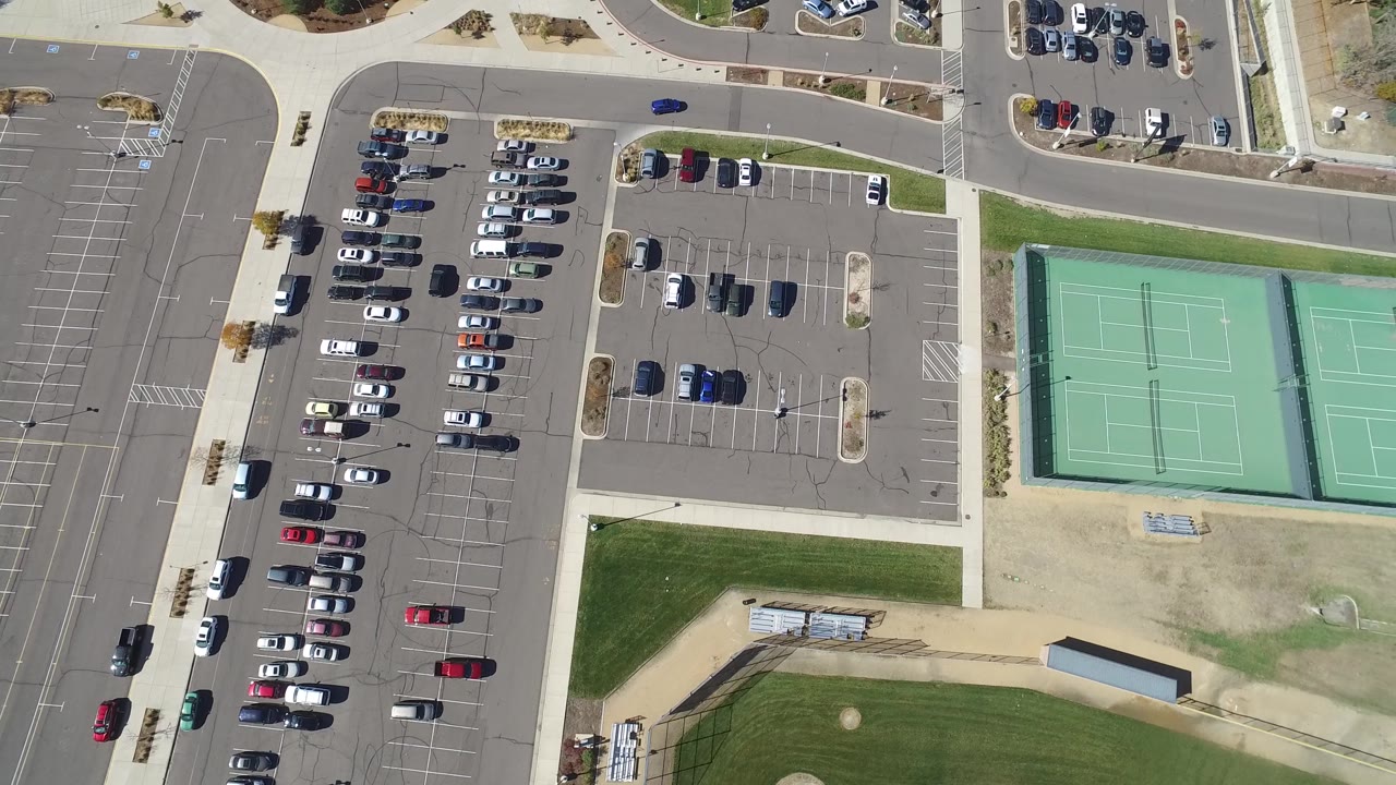 High overhead view of an organized parking area next to green tennis courts and park paths.