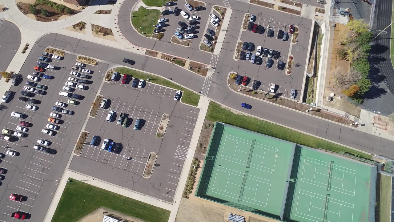 Second overhead frame in Hidden Lake, Colorado with a small blue car on the road, parked vehicles in lots, tennis courts at lower right, and no visible people.
