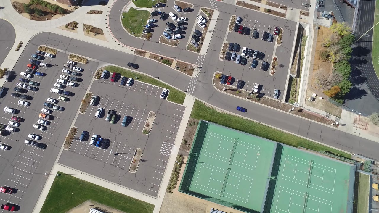 Top-down view of a blue car passing parking areas near tennis courts.
