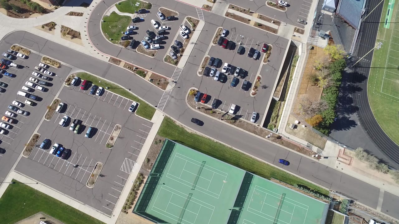 The next Hidden Lake, Colorado frame keeps the tennis courts at the lower edge, a paved road through the middle, and parked vehicles clustered in several lots, with no clearly visible people.