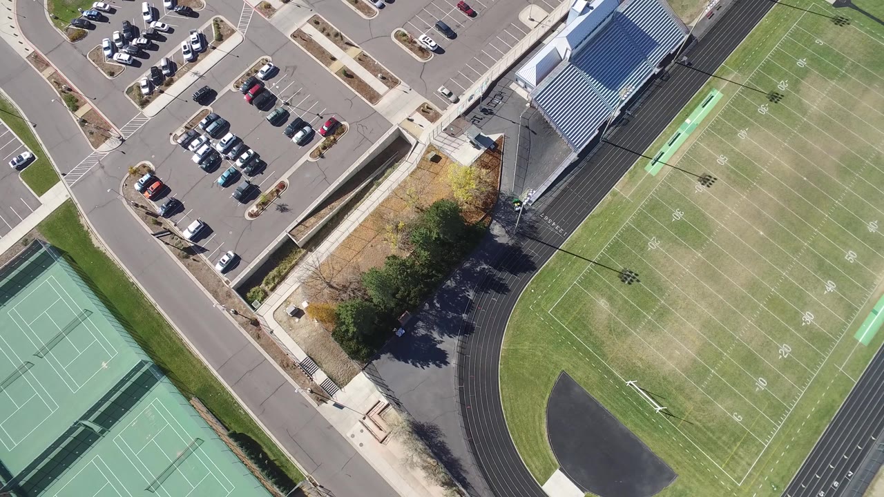 Second overhead frame in Hidden Lake, Colorado with the parking area high in frame, bleachers beside the track, tennis courts at lower right, field markings, and no visible people.