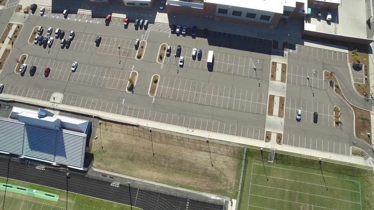 Top-down aerial view of a shopping mall parking lot and sports fields.