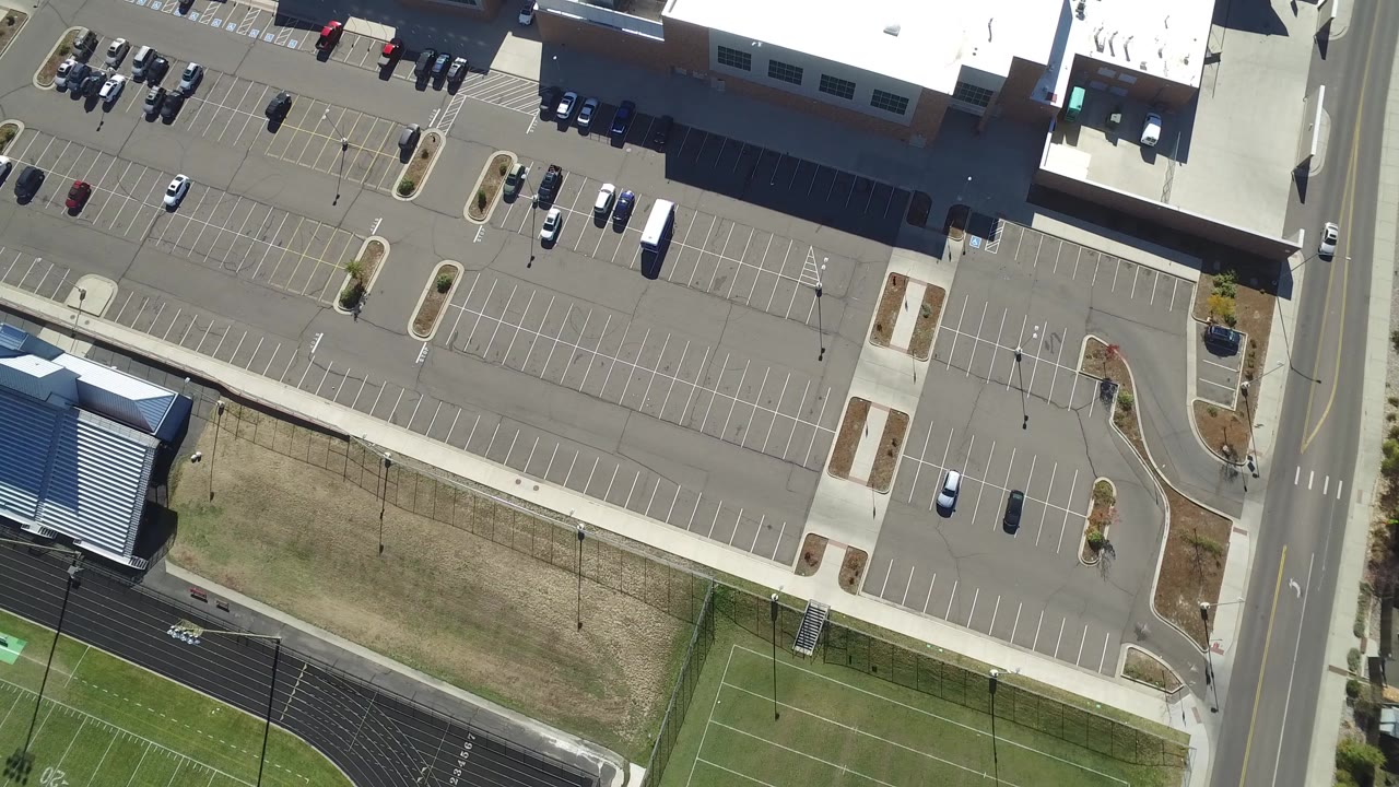 Overhead parking lots, road, and athletic fields beside low buildings.