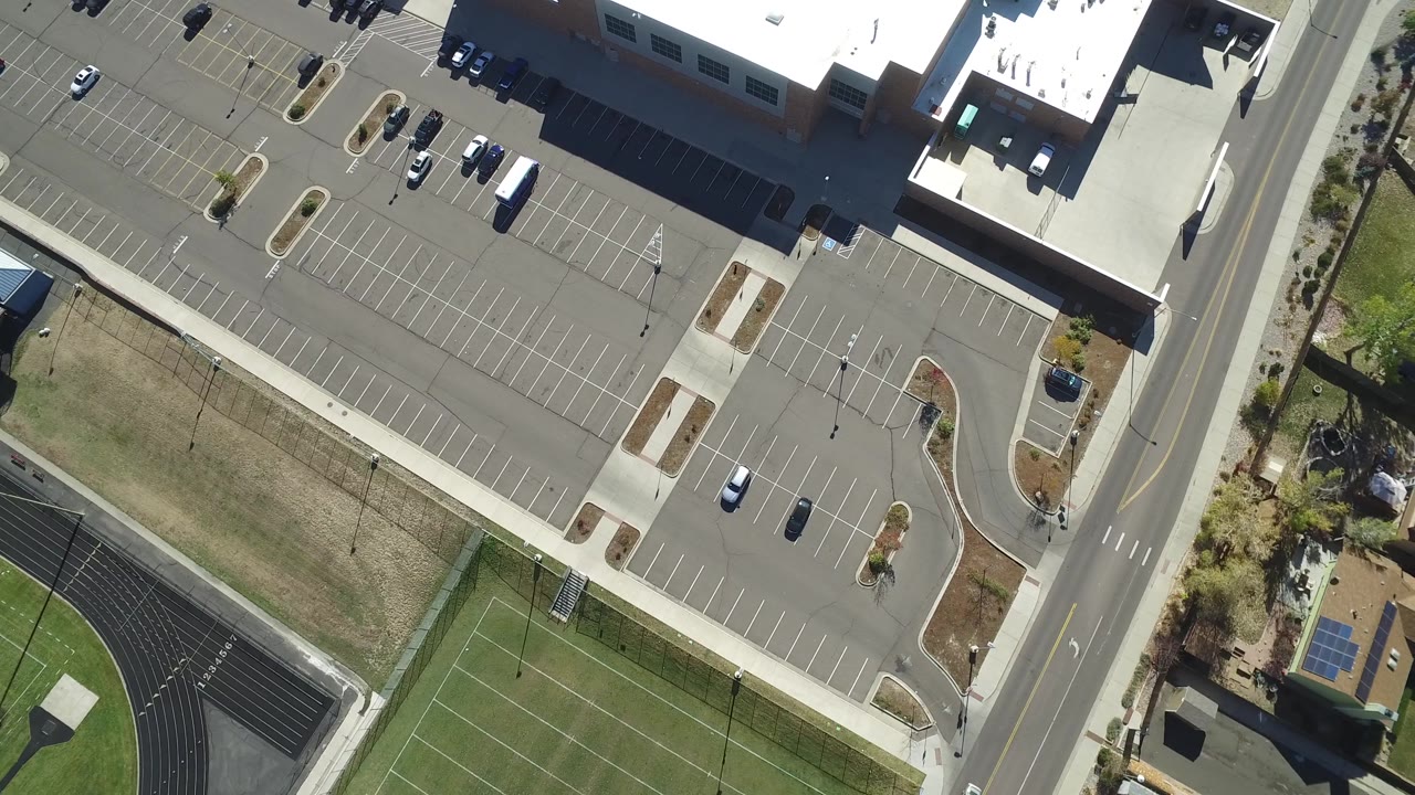 Aerial view of a road beside a parking lot with sports fields and houses nearby.