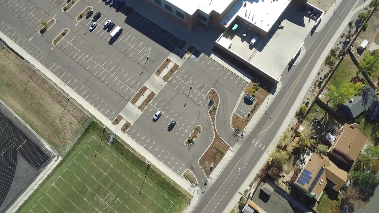Top-down aerial view of a sports field, road, parking lot, and houses.