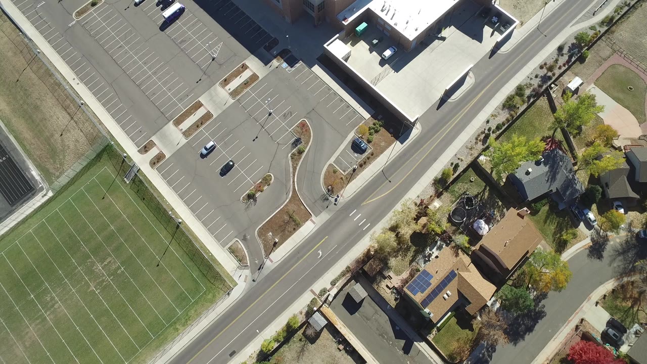 Near-vertical aerial frame in Hidden Lake, Colorado showing a striped green sports field, diagonal road, parking lot, sidewalks, trees, and private homes with no clearly recognizable people visible.