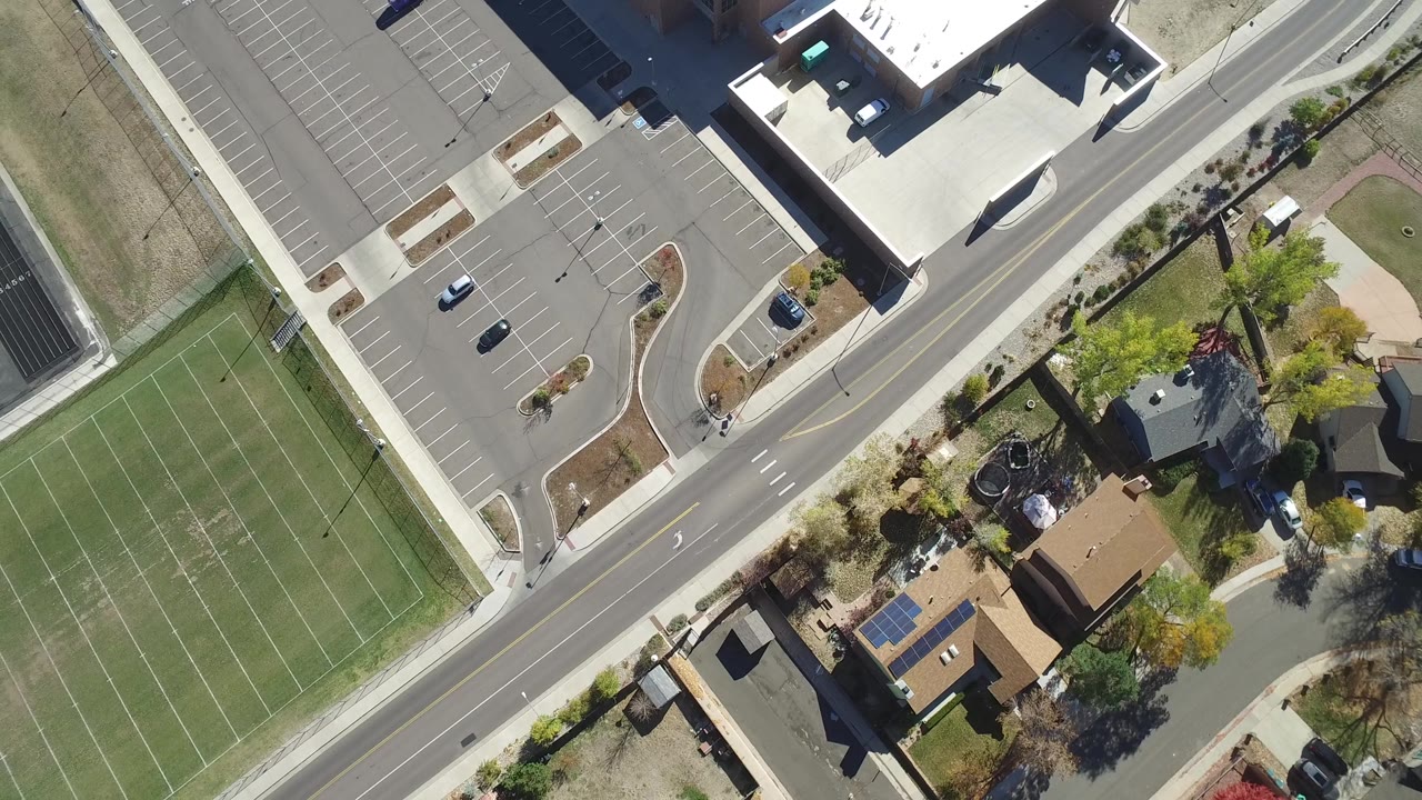 Top-down view of a road crossing between parking lots, buildings, courts, and homes.