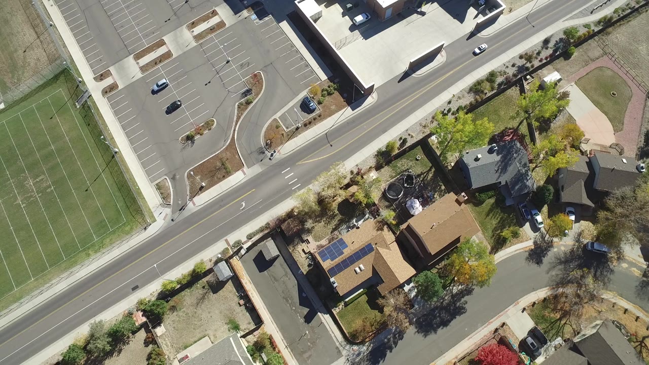 Overhead view of a road, parking lot, athletic field, and nearby houses.