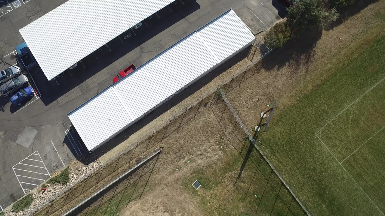 Overhead view of white carports beside a parking lot and grass field.