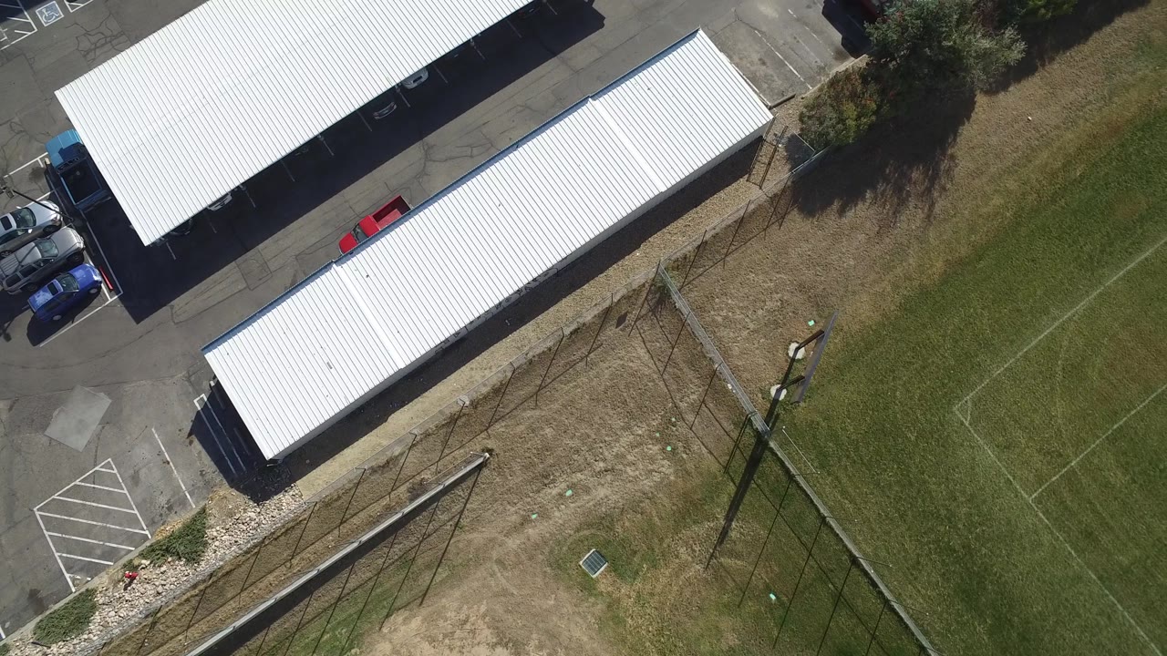Hidden Lake, Colorado aerial view with two long white carport roofs, parked vehicles at the lot edge, fence lines across grass, and no visible people.