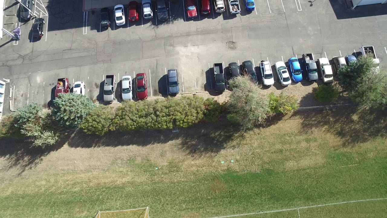 Overhead parking lot beside trees and a grass field.
