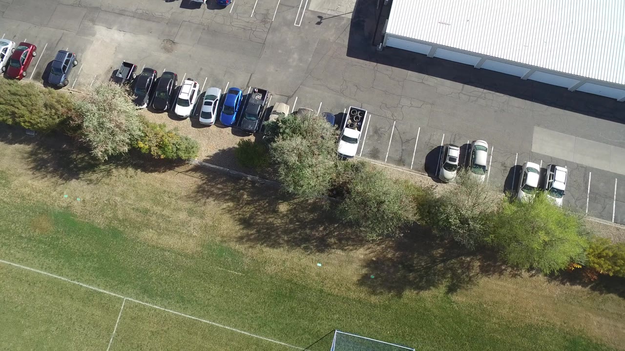 High aerial view of a parking lot row, trees, and open grass with field lines.