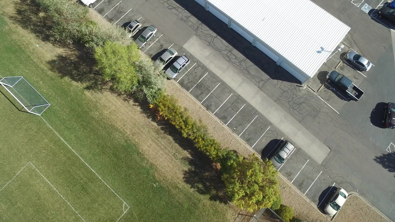 Overhead parking lot beside a white-roofed building and grass field.
