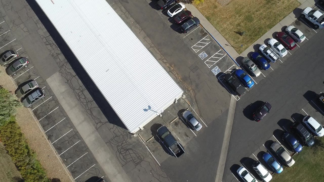 In Hidden Lake, Colorado, a black car appears in the open driving lane of a sunlit parking lot near the white-roofed building, with no visible people.