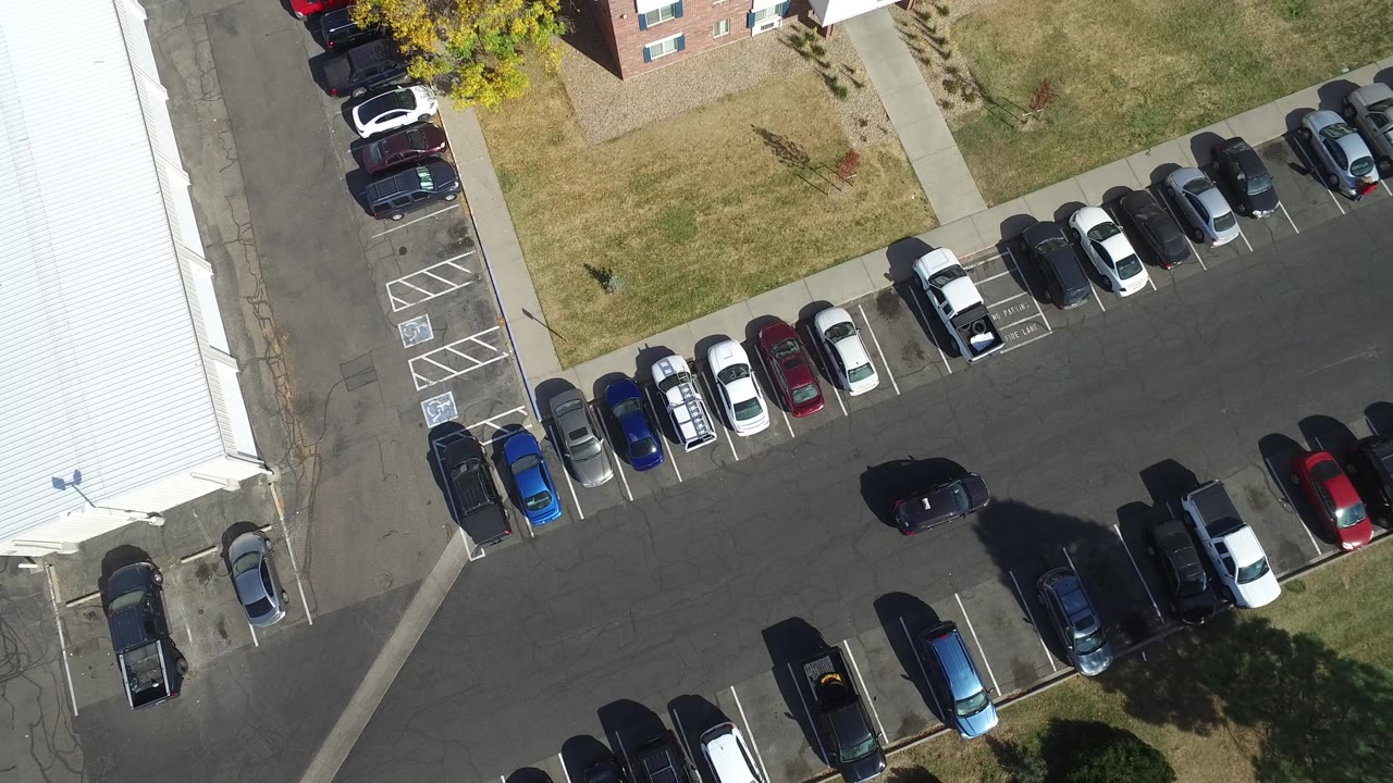 Aerial view in Hidden Lake, Colorado with the black car slightly farther along the parking lane, flanked by compact parked vehicles, sidewalks, grass, and no visible people.