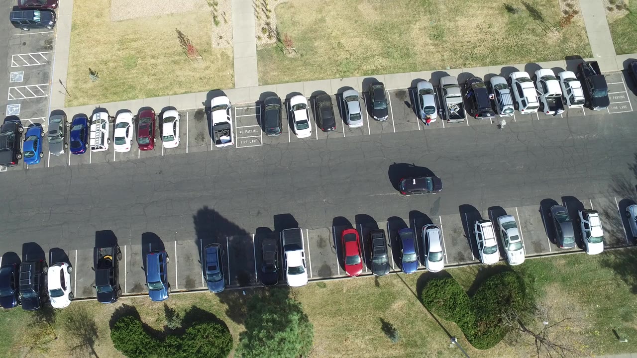 Overhead view of a crowded parking lot with a dark car in the drive lane.