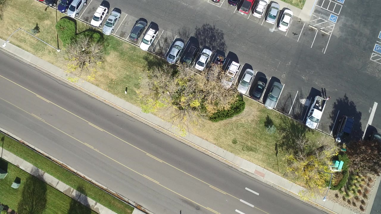 Opening frame of Hidden Lake, Colorado from above, showing a row of parked cars, a two-lane road, sidewalks, trees, grass, and no visible people.