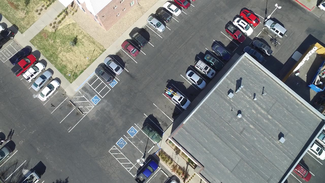 Overhead frame in Hidden Lake, Colorado with the gray roof lower right, rows of parked vehicles along the asphalt, accessible stalls near the sidewalk, and no visible people.