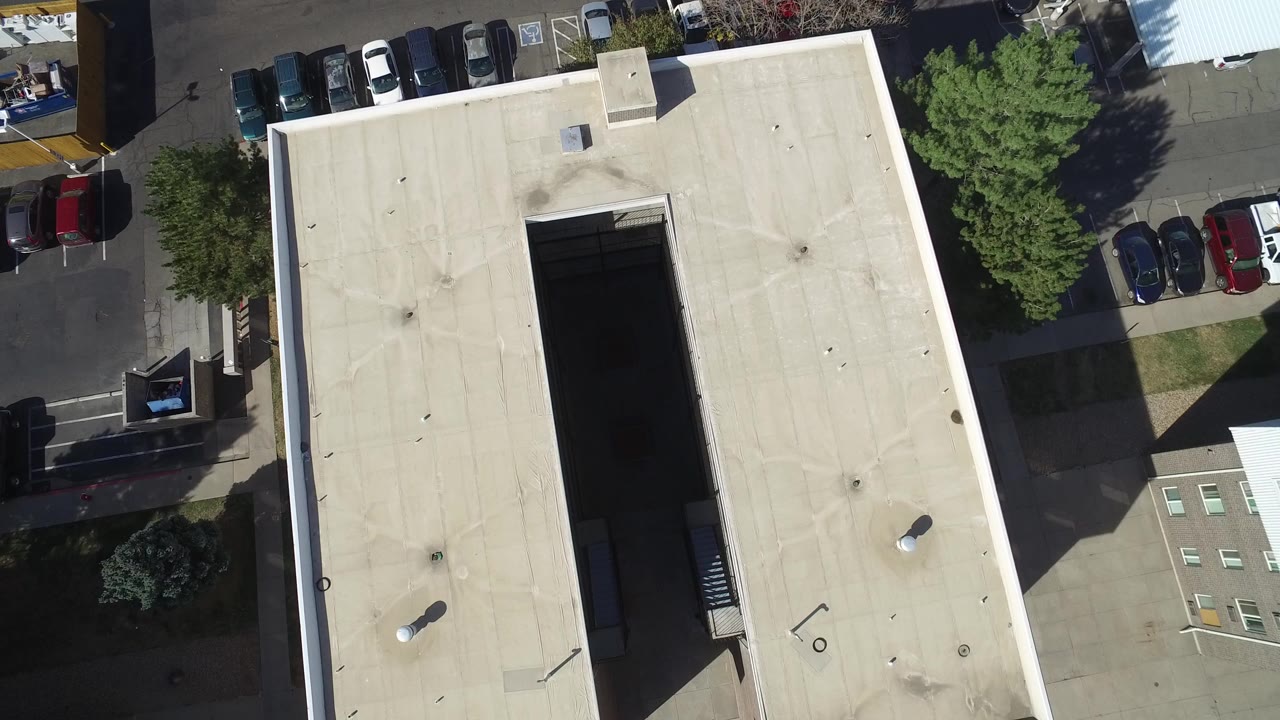 Overhead view of a flat warehouse roof beside a parking lot.