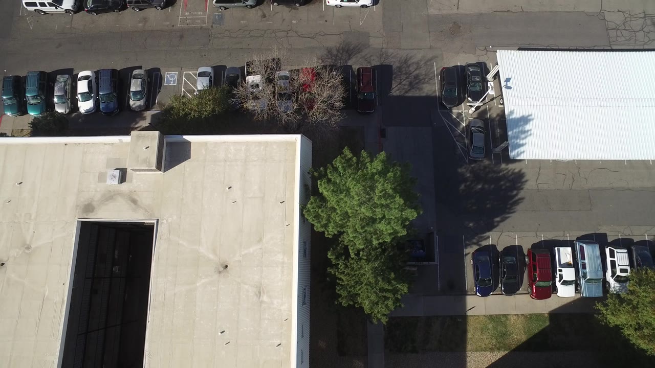 Top-down view of a warehouse roof, parked vehicles, road, and trees.