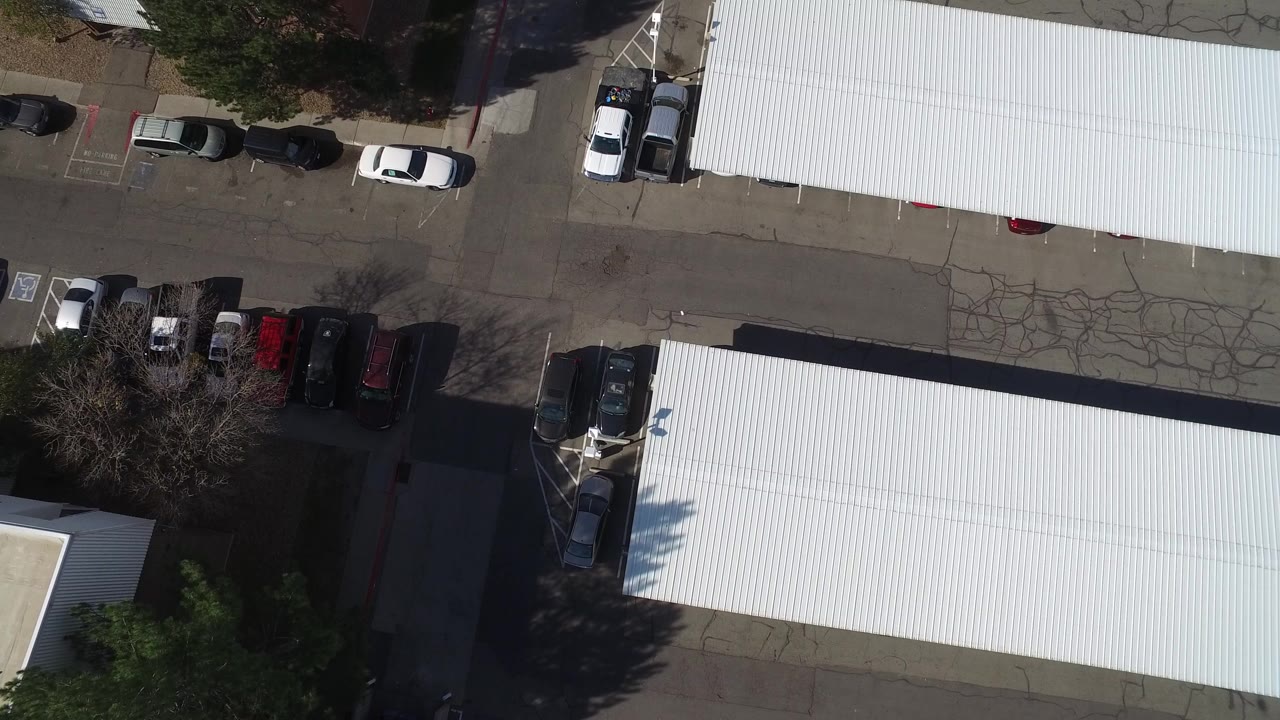 Overhead view of white-roof buildings and parked vehicles beside an asphalt lot.