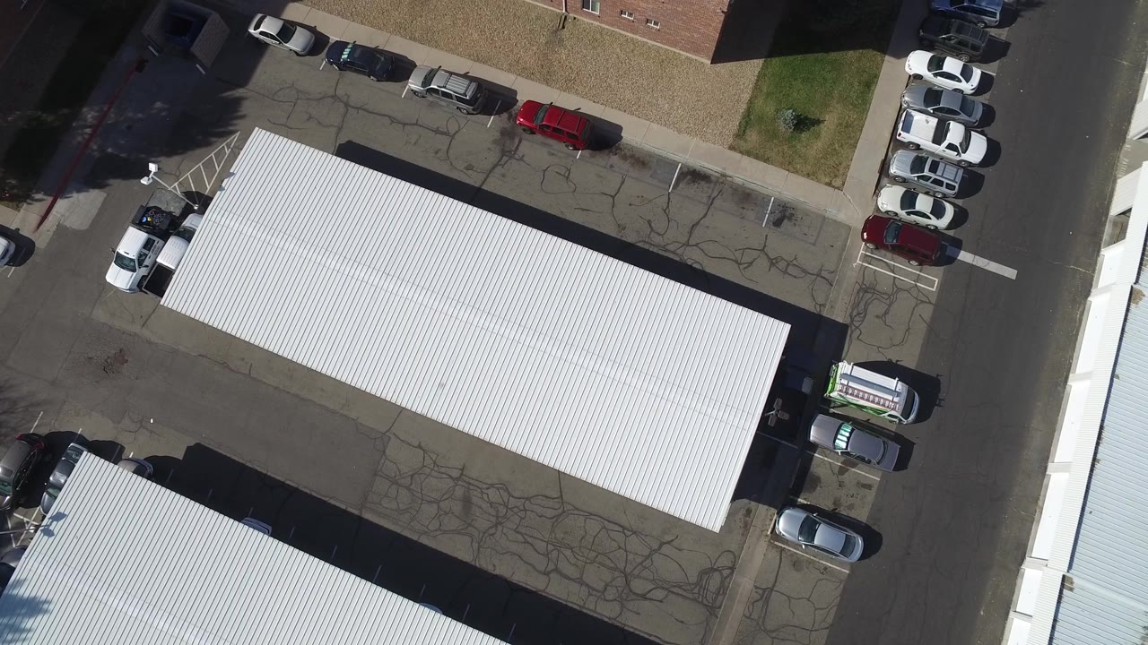 Top-down view of a parking area, white roof, road, and rows of cars.