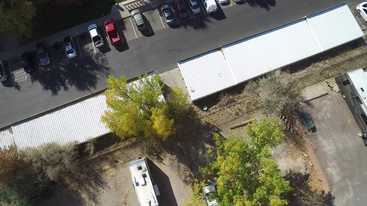 Overhead aerial frame in Hidden Lake, Colorado showing white metal roofs, a parking row, trees, trailers, and no visible people at the start of the clip.
