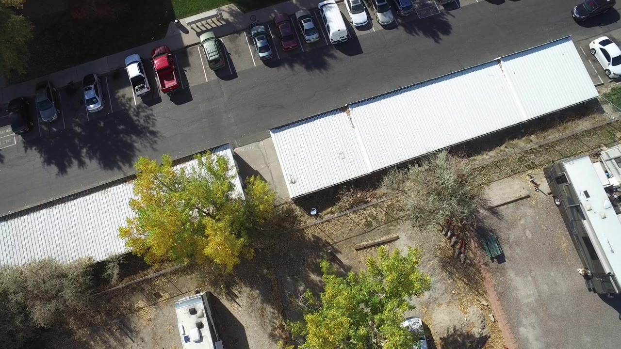 Top-down view of commercial roofs, parked cars, trailers, and trees.