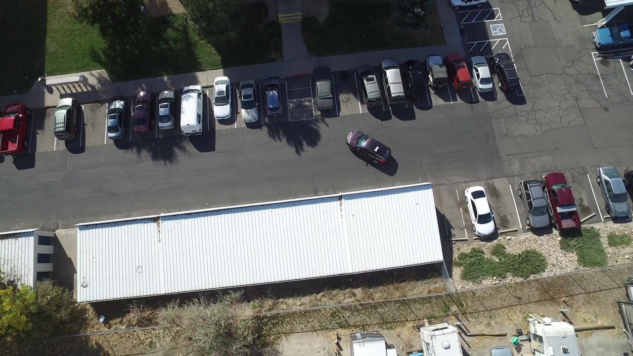 Top-down parking lot with rows of cars and a long white roof.