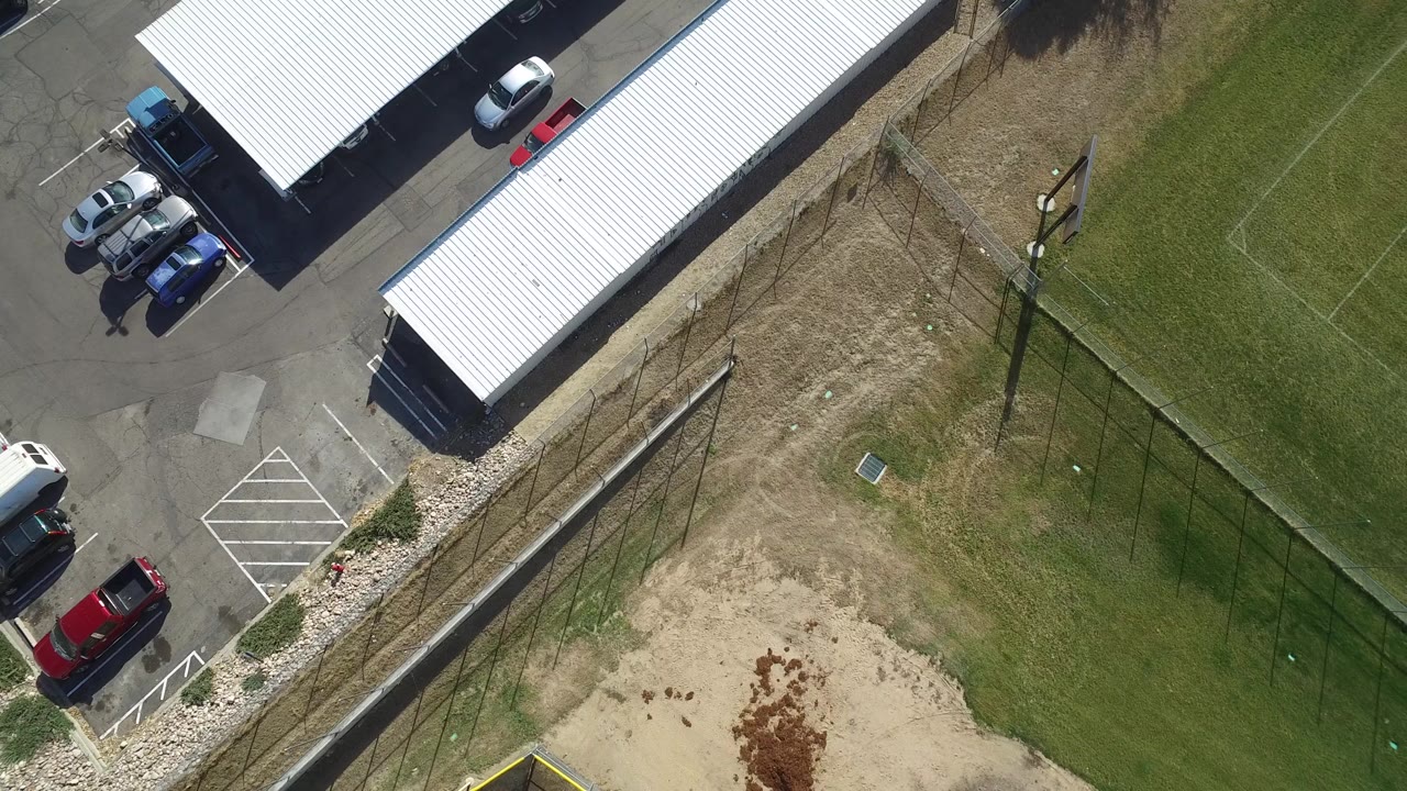 At 0:02, the aerial frame in Hidden Lake, Colorado shows more of the parked cars near the white-roofed structures, with the fence and open field still visible and no visible people.