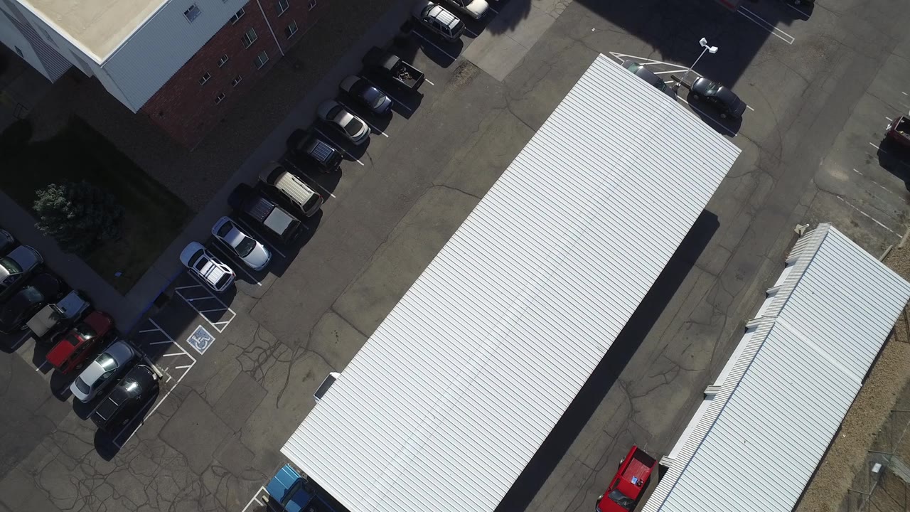 A Hidden Lake, Colorado aerial frame shows the white-roofed structure centered between parked cars, pavement markings, and neighboring commercial rooflines with no visible people.