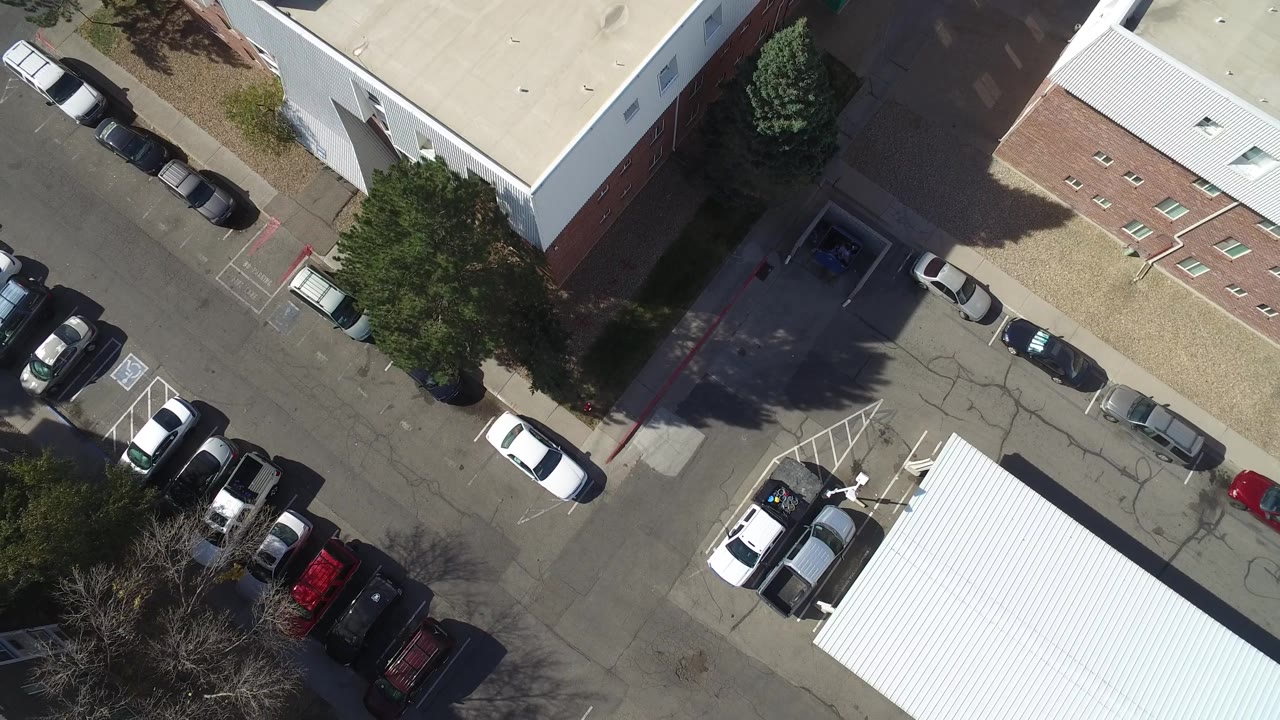 Hidden Lake, Colorado aerial frame with a white car near the center, rows of parked vehicles beside commercial buildings, and no visible people.