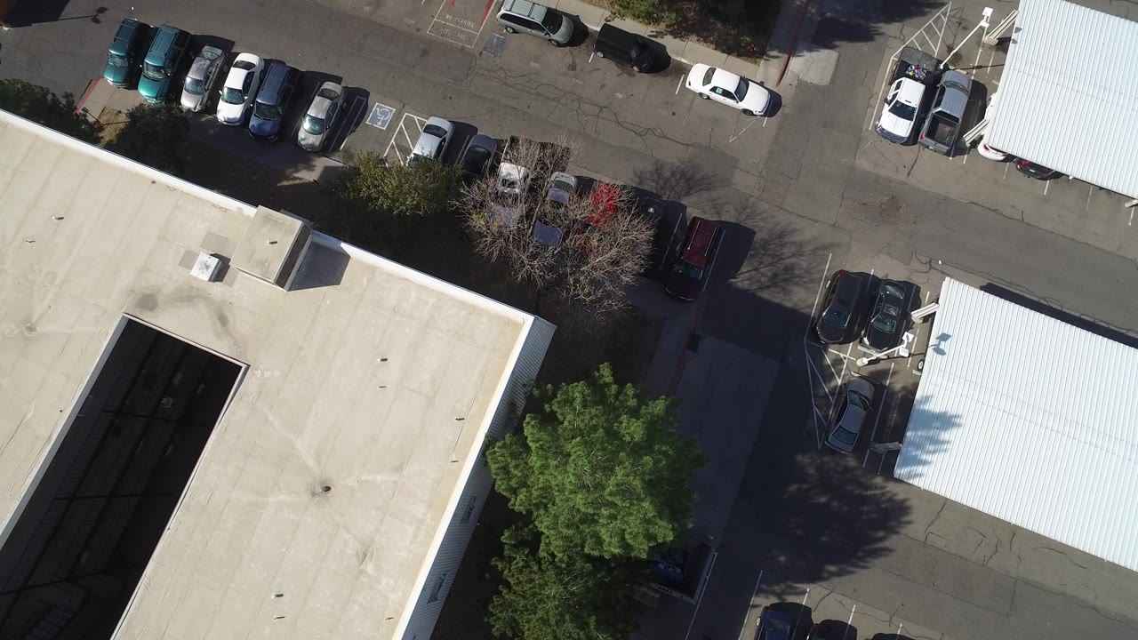 High overhead frame from Hidden Lake, Colorado showing a tan flat roof, adjacent parking rows, gray pavement, trees, and no visible people.