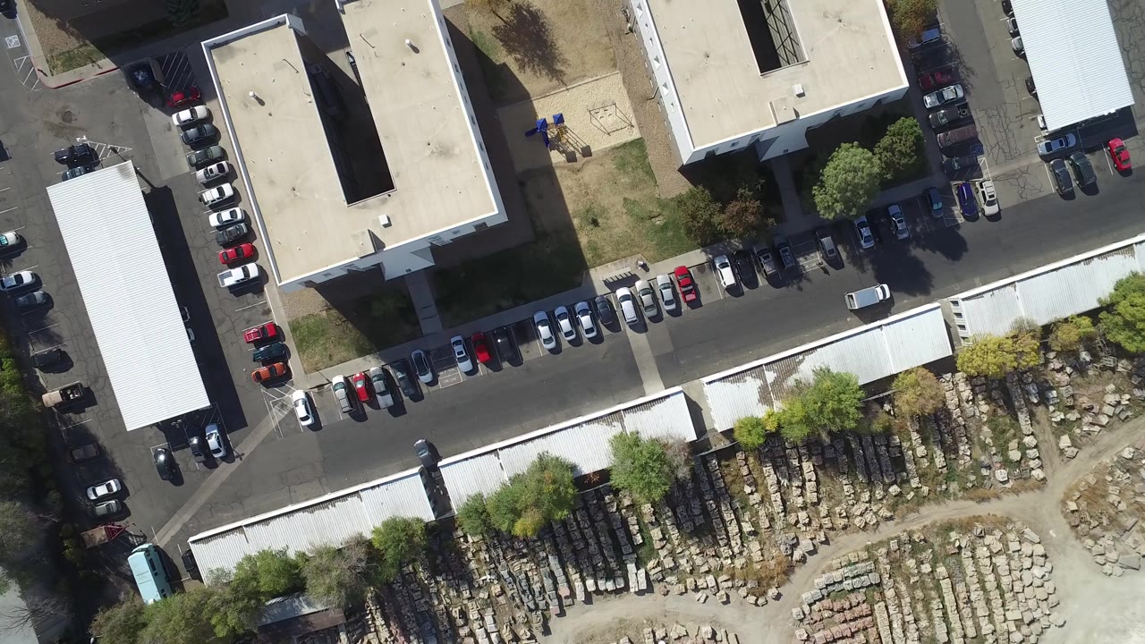 Overhead view of flat-roofed buildings, parked cars, and stacked materials.